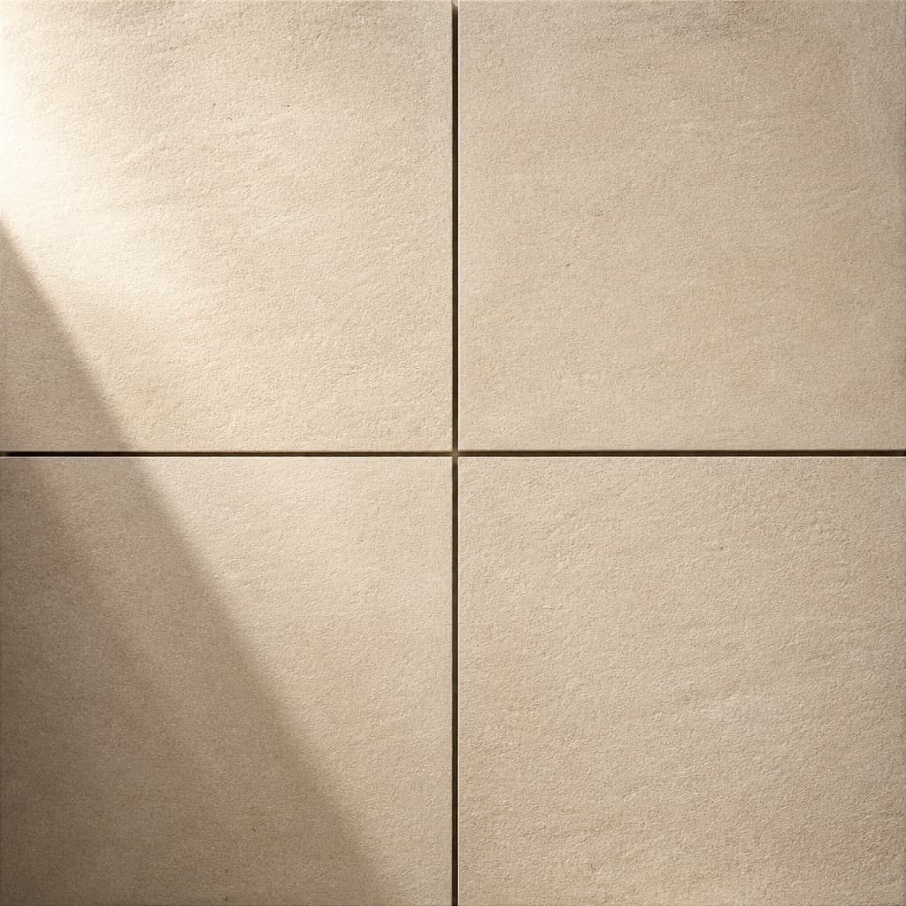 Four square brushed limestone tiles laid in a two-by-two grid, seen from above with raking light across the pale sand surface
