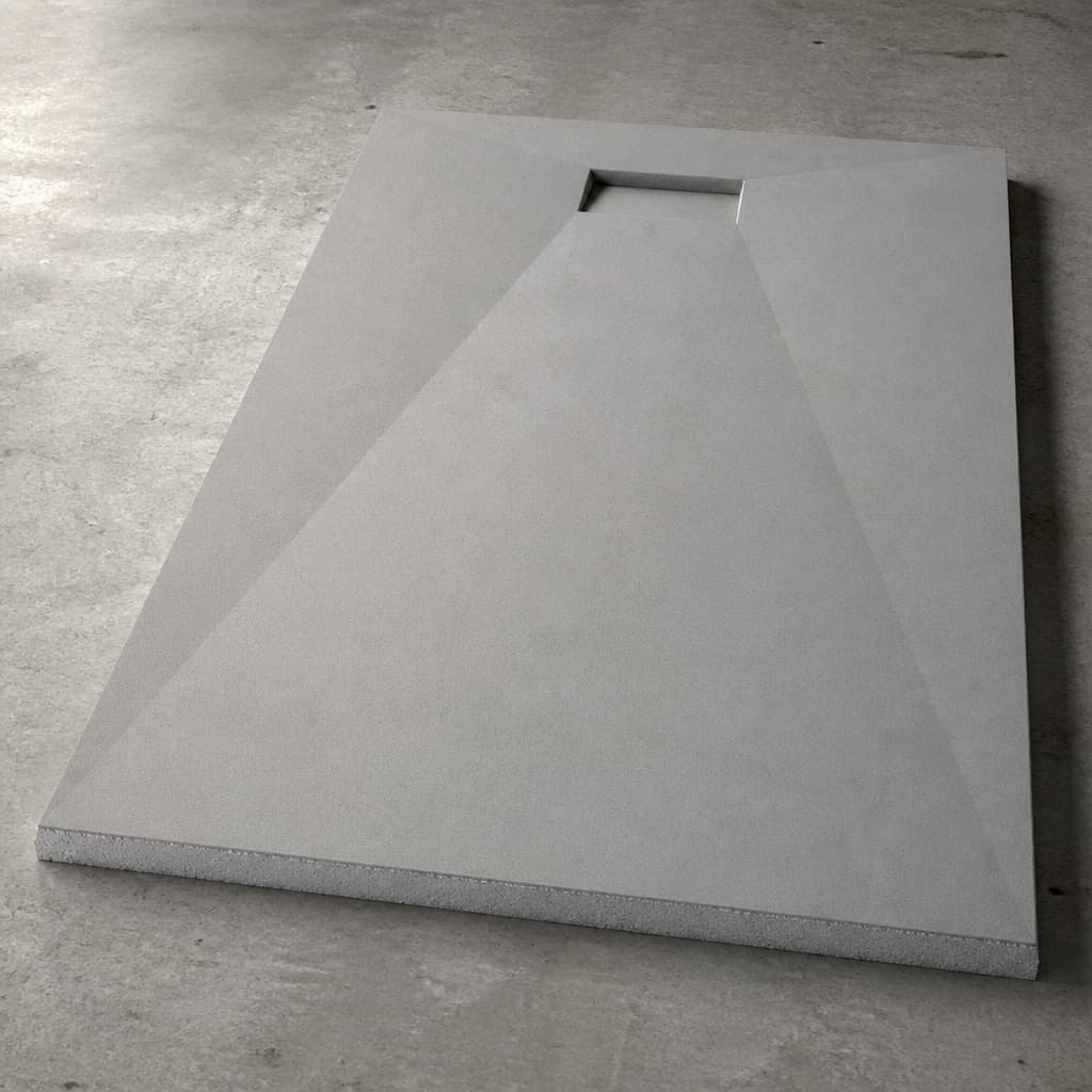 A cement-coated pre-sloped shower pan seen from above, its facets falling to a rectangular drain opening at one end, foam core visible at the cut edge